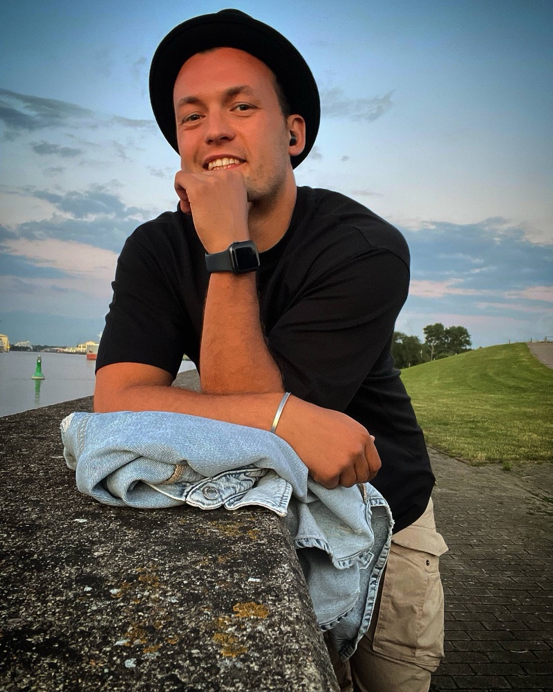 Philipp Mertens lächelnd mit Hut am Weserufer